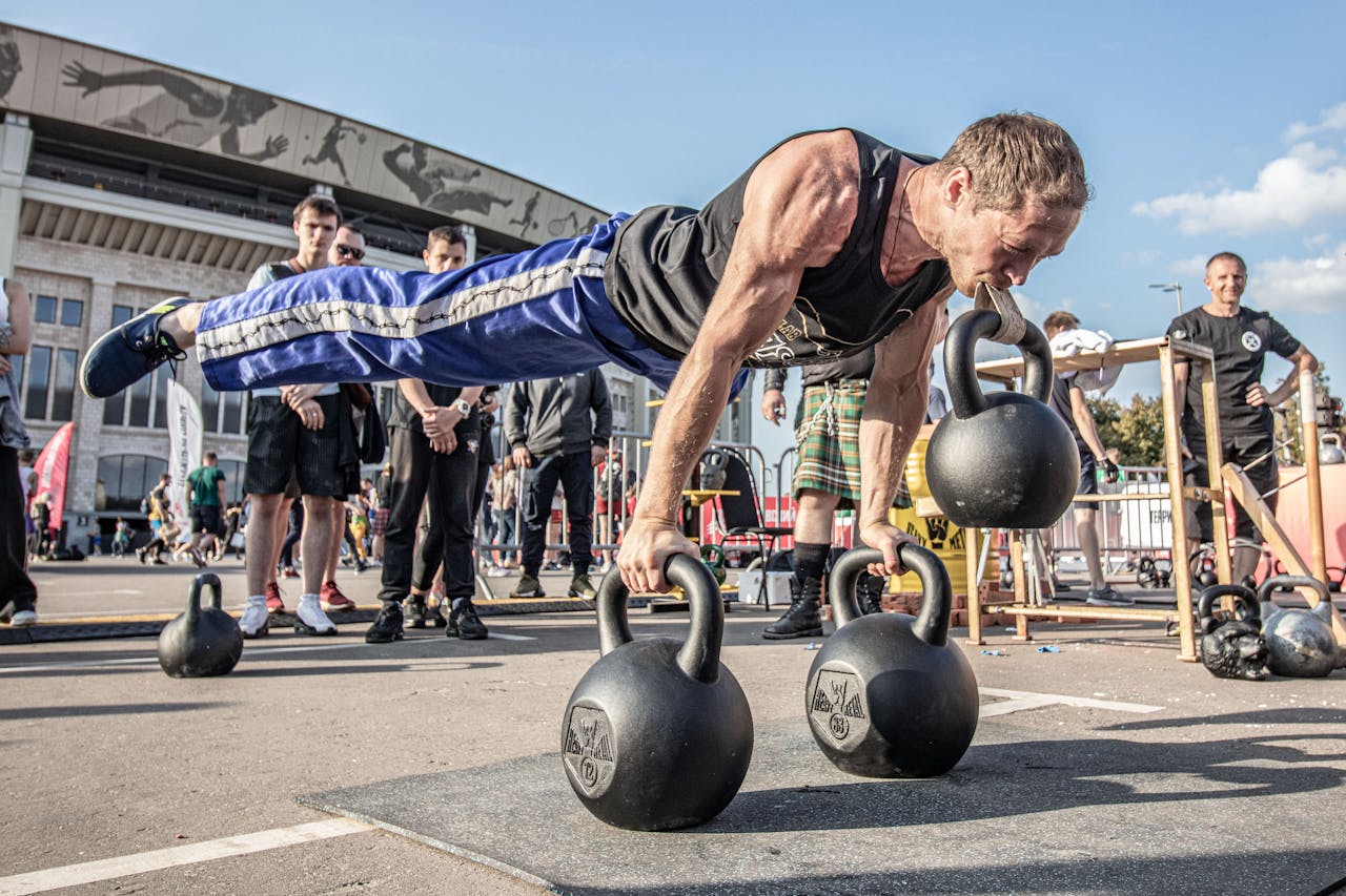 Man performs a balance exercise with kettlebells at an outdoor fitness event.