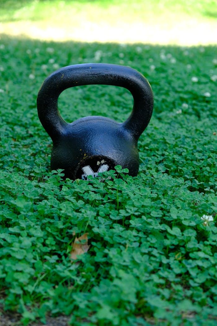Black kettlebell resting on lush green clovers outdoors, symbolizing strength and nature.